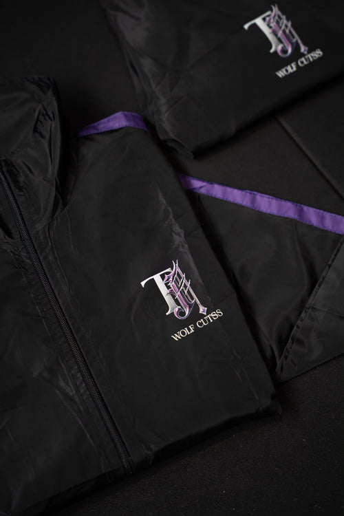 Black TJ Wolf Cutss tracksuit jacket and pants folded flat, showing purple side stripe and chest logo