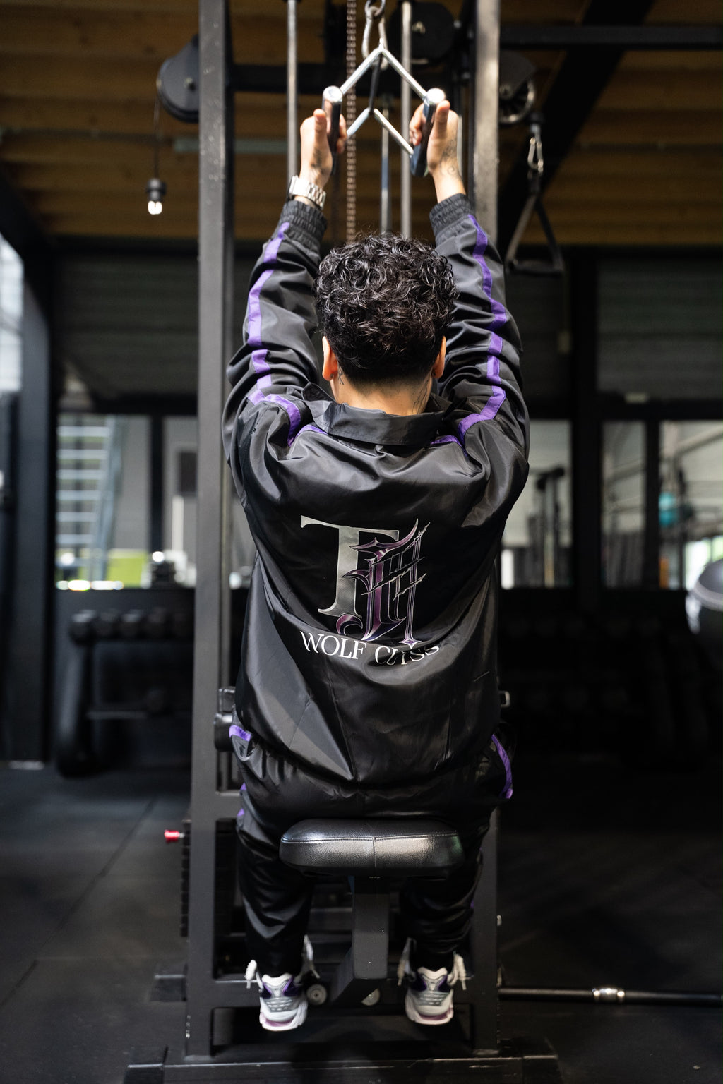 Model standing in the black TJ Wolf Cutss tracksuit with hands in pockets, chest logo visible