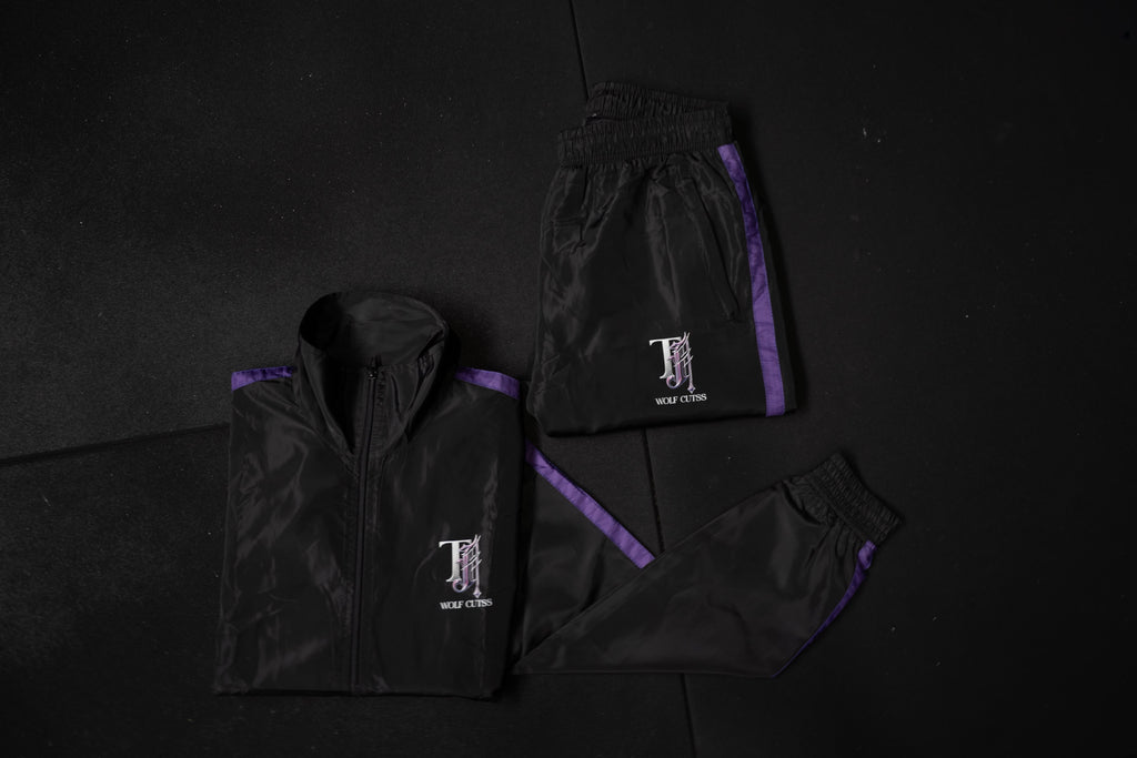 Black TJ Wolf Cutss tracksuit jacket and bottoms flat lay on a black background