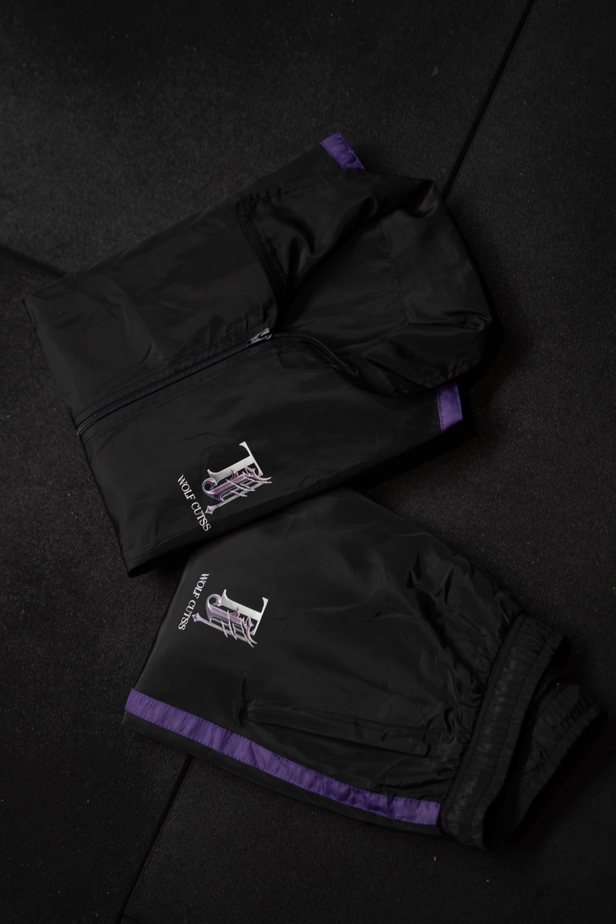 Folded black TJ Wolf Cutss tracksuit set showing purple trim and sleeve logo
