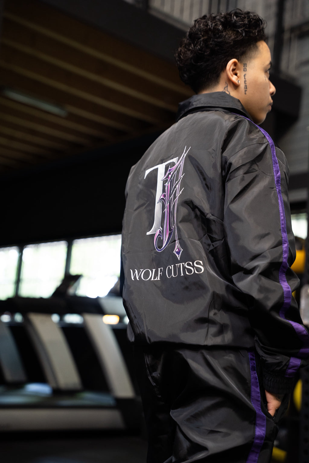 Side profile of a model wearing the TJ Wolf Cutss tracksuit jacket in a gym